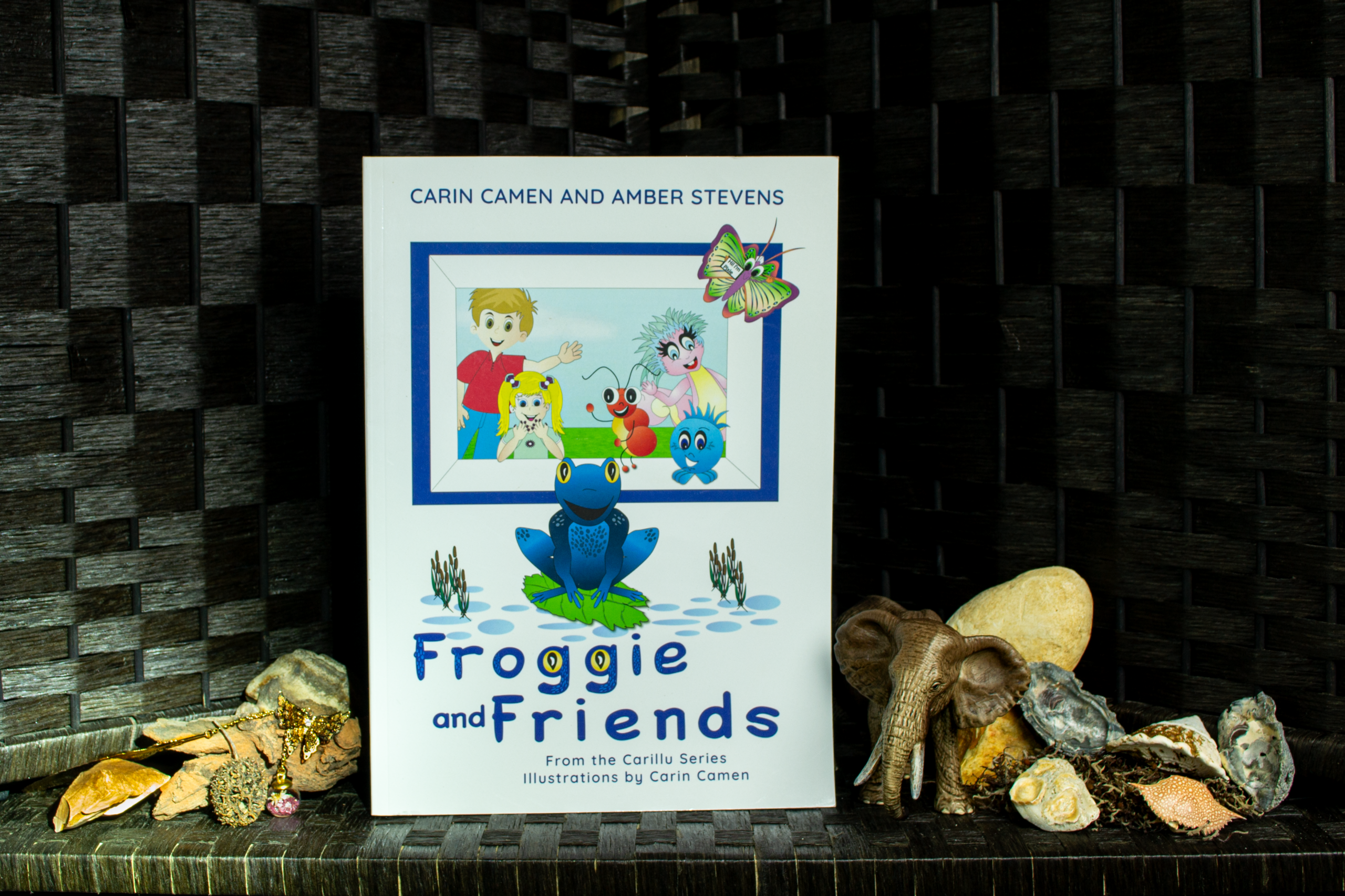 Froggie and Friends children’s book from the Carillu series, displayed with an elephant figurine, rocks, shells, and natural objects.