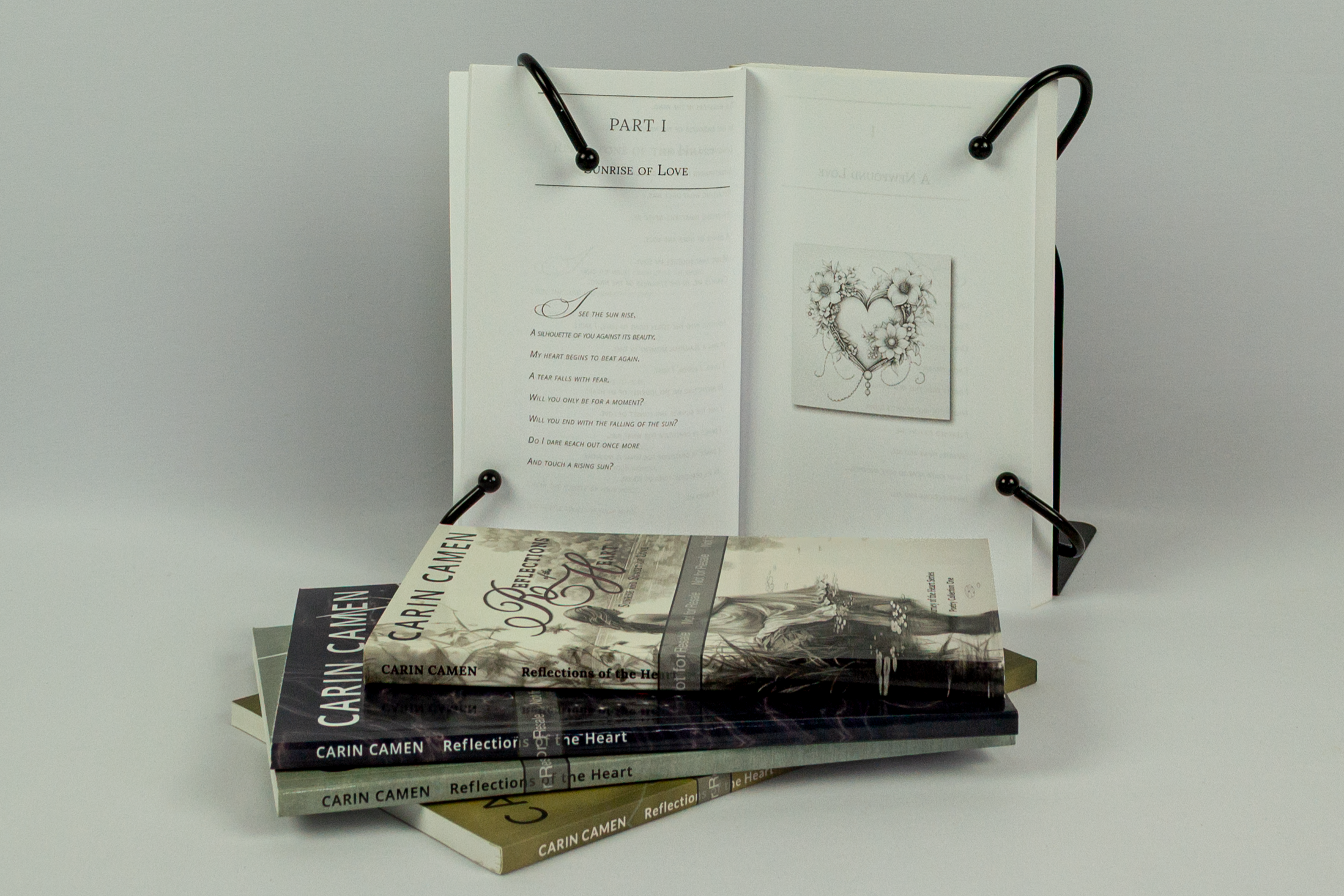 Open Reflections of the Heart poetry book displayed behind four stacked editions, showing an illustrated poetry spread by Carin Camen.