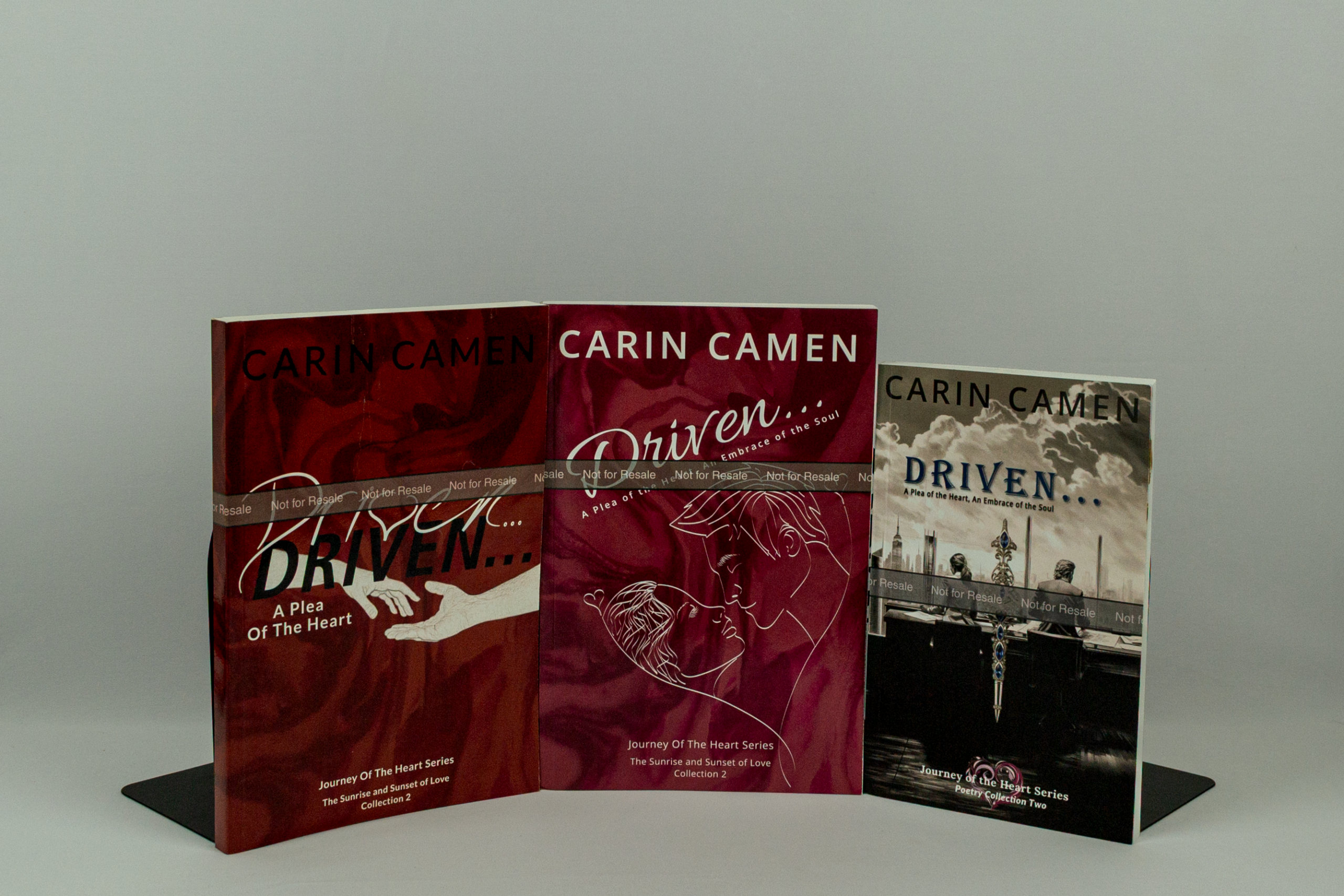 Three physical editor proof editions of Carin Camen’s Driven... poetry collection displayed together, showing the evolution of the book’s cover design.
