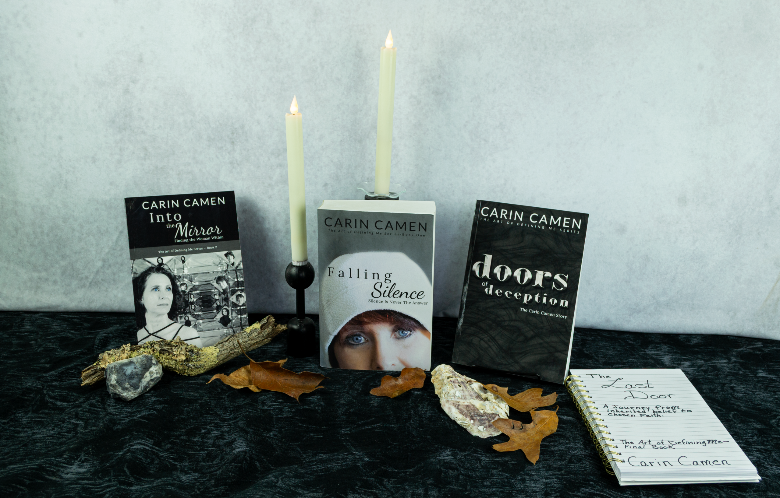 The Art of Defining Me memoir series by Carin Camen, featuring Into the Mirror, Falling Silence, doors of deception, and a notebook representing the planned final book, The Last Door.